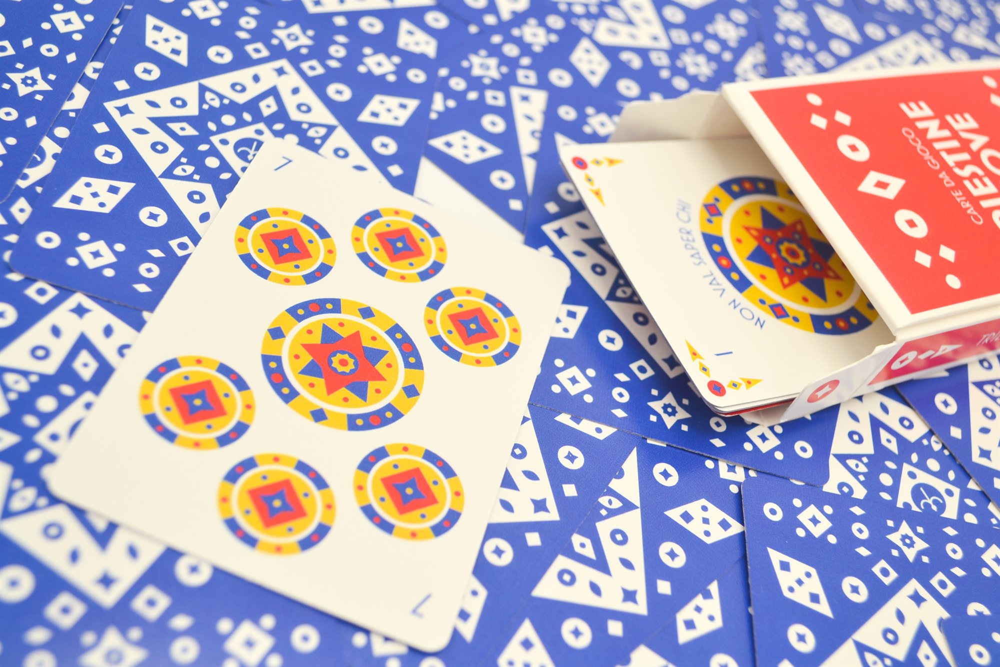 An open red Carte Triestine Nuove box beside a spread of cards, with the seven of coins face up in the foreground