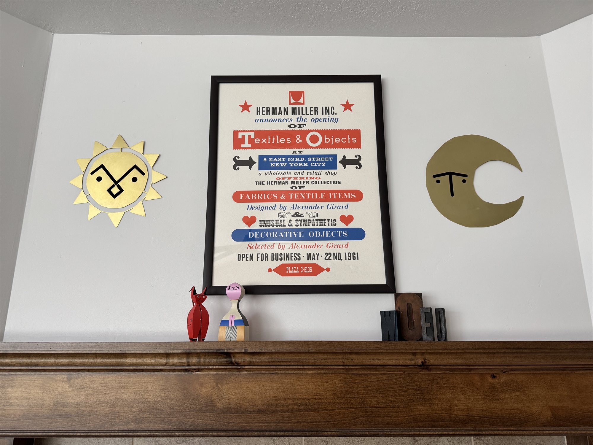 Another view of the brass sun and moon flanking the framed Herman Miller poster above the mantel, with carved figures and letterpress blocks arranged below