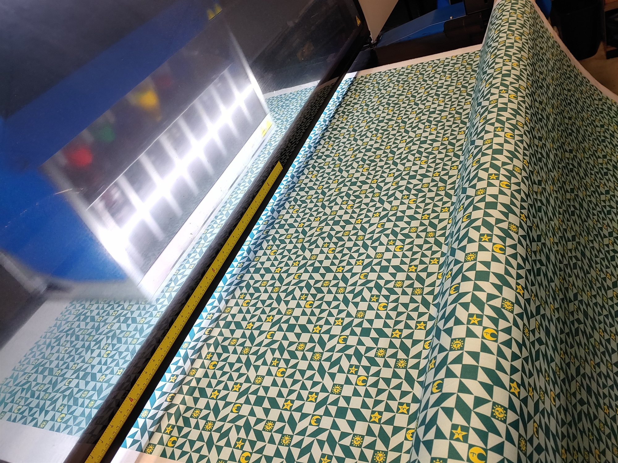 The green and white colorway coming off a large-format printer, sun, moon, and star icons speckled across the triangle pattern