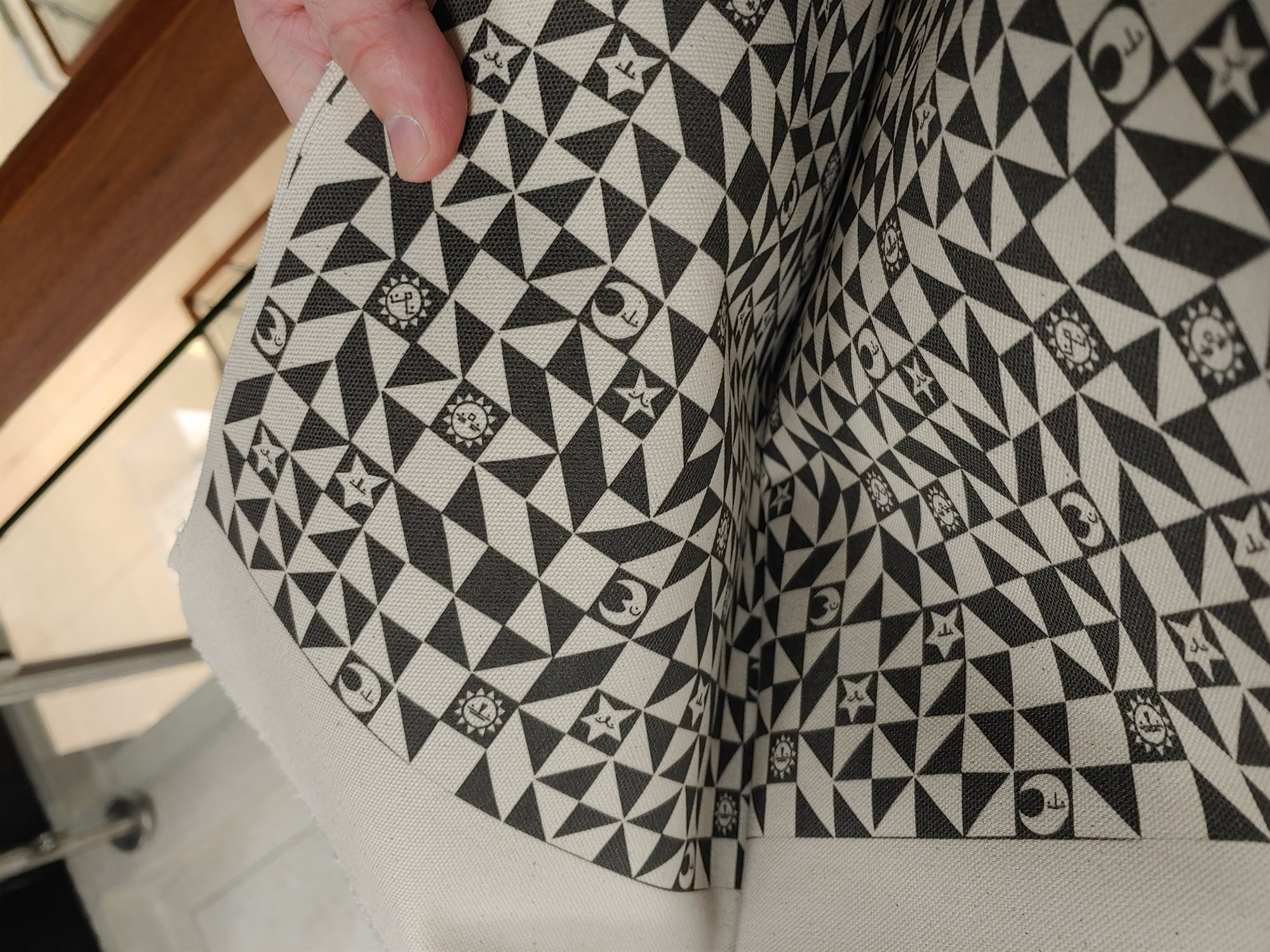 A hand holding up a folded length of the black and white colorway, showing the printed canvas texture up close
