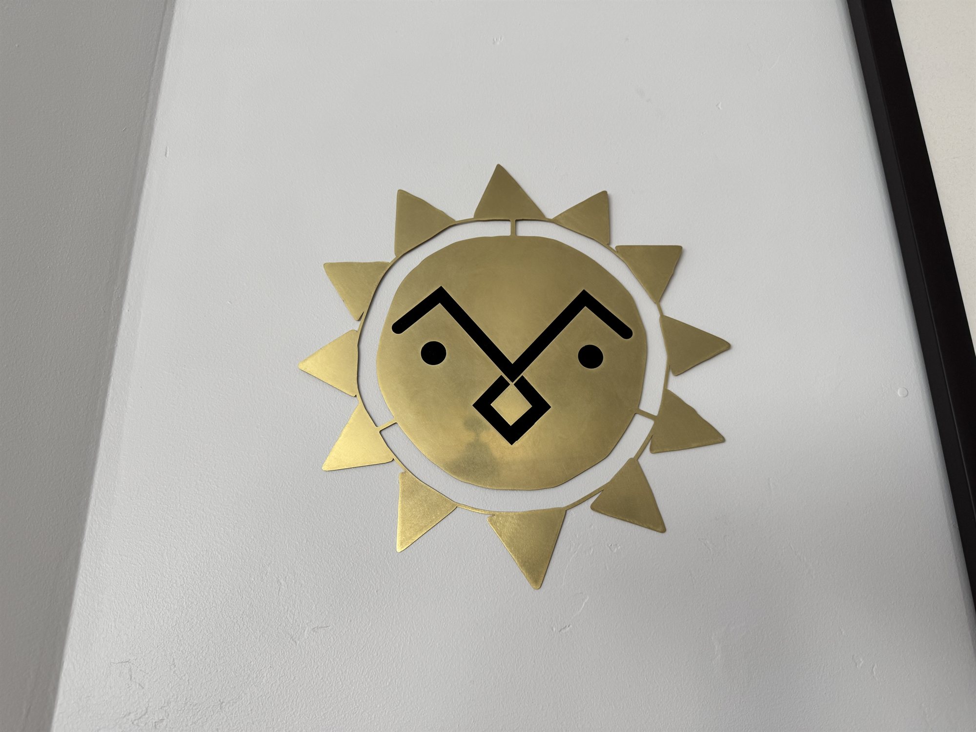 Close-up of the brass sun piece on the wall, its triangular rays and grumpy cutout face backed in black velvet to make the features stand out