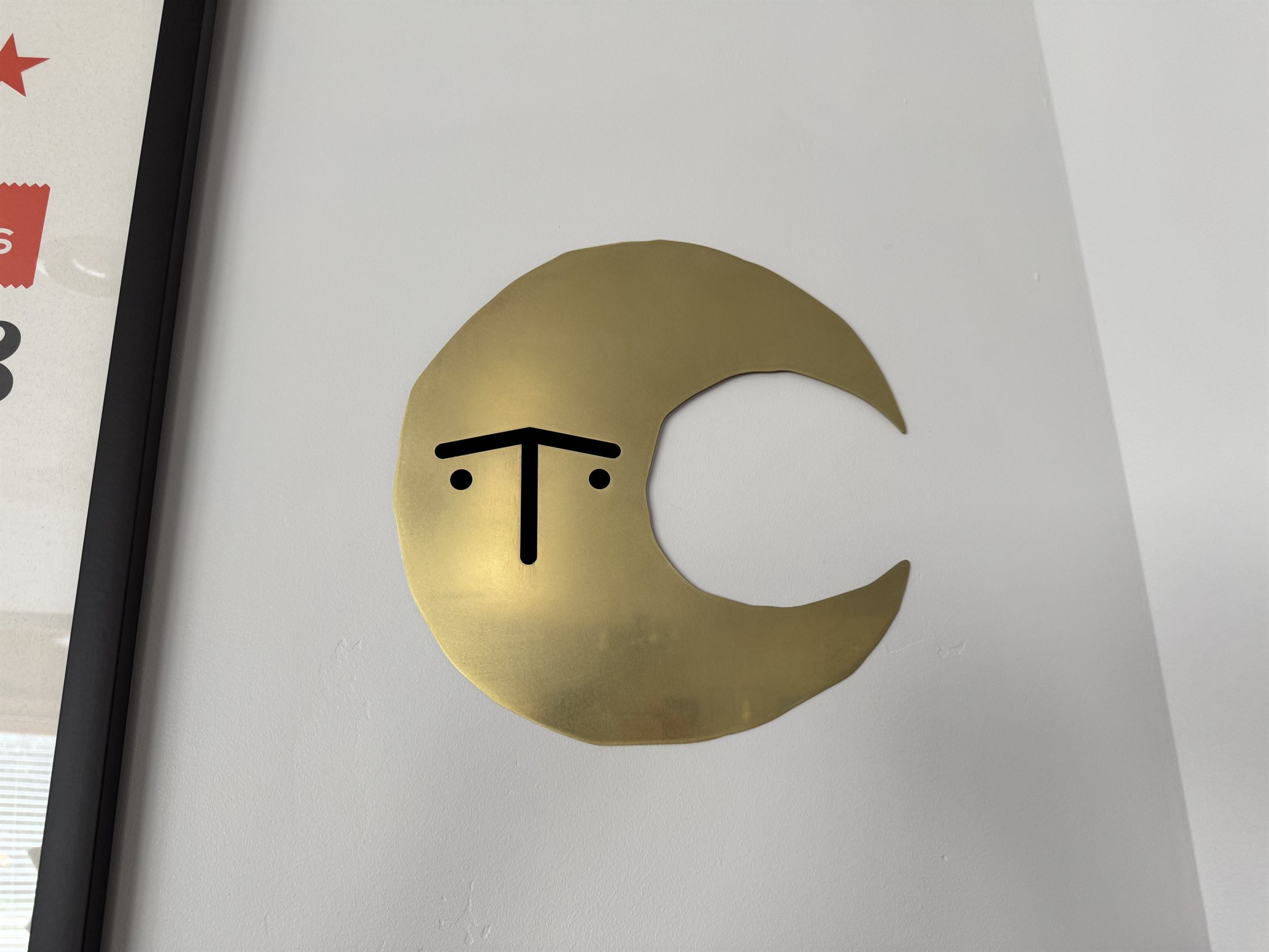 Close-up of the brass crescent moon piece on the wall, its grumpy T-shaped cutout face backed in black velvet to make the features stand out
