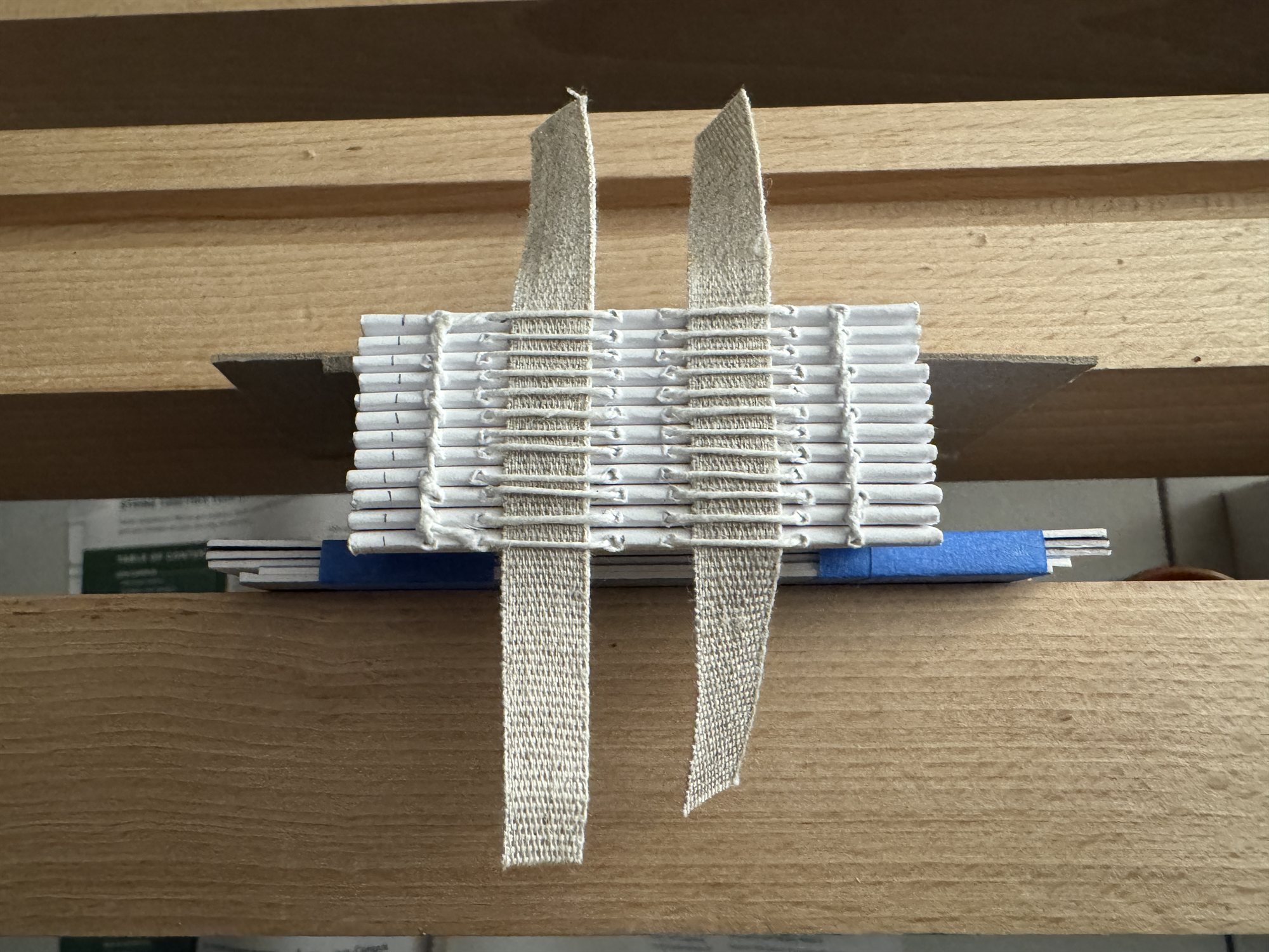 A hand-sewn text block on a wooden sewing frame, folded signatures stitched onto cloth sewing tapes