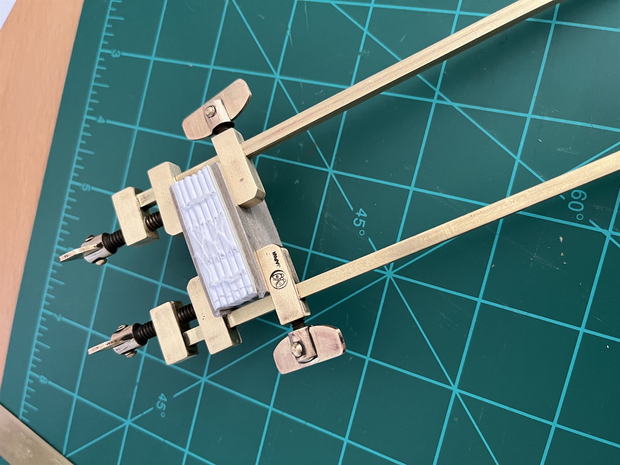 A small book block clamped in a brass finishing press for rounding and backing, resting on a cutting mat