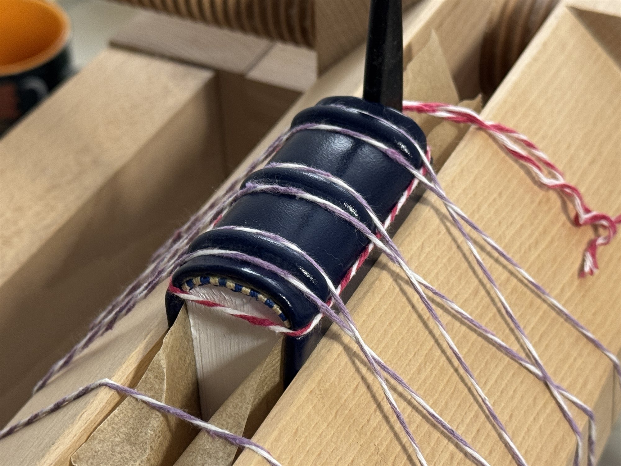 A navy leather spine laced onto its boards on the finishing press, cord wrapped tightly around the raised bands