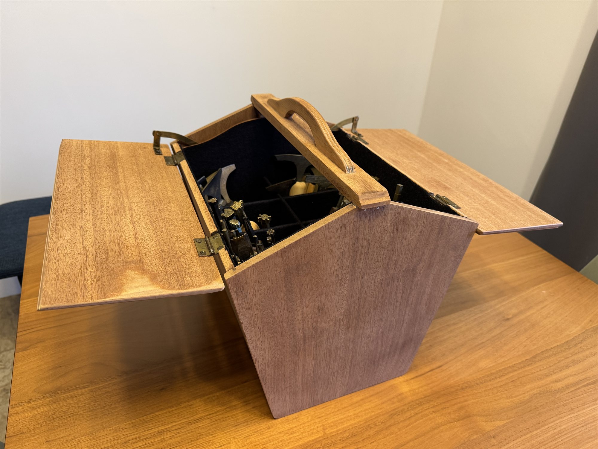 A wide view of the open sewing box with both lids spread flat, rows of tools and stamps packed inside