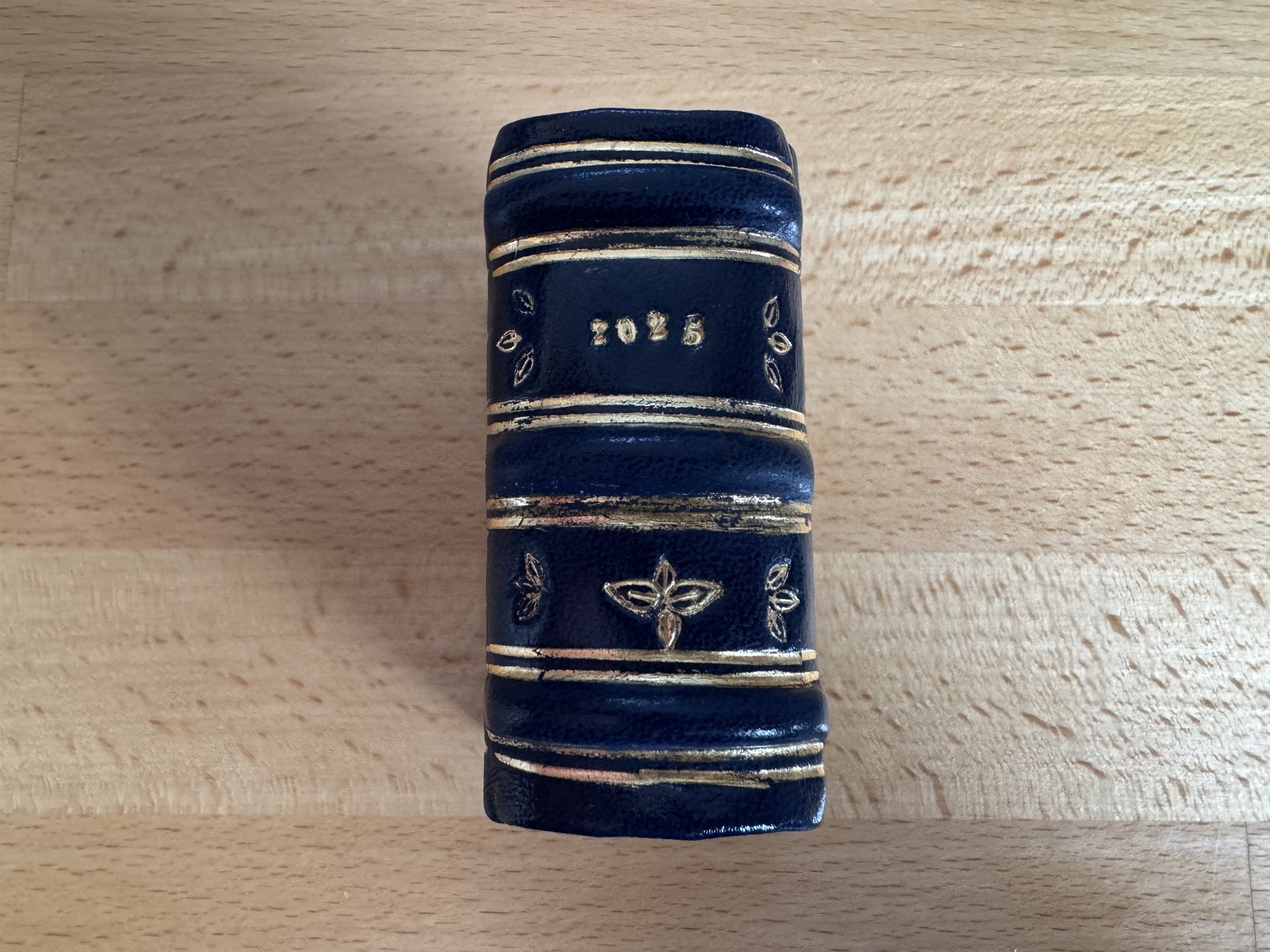 The spine of a green leather book gold-stamped with the year 2025 between floral tooling and gilt bands