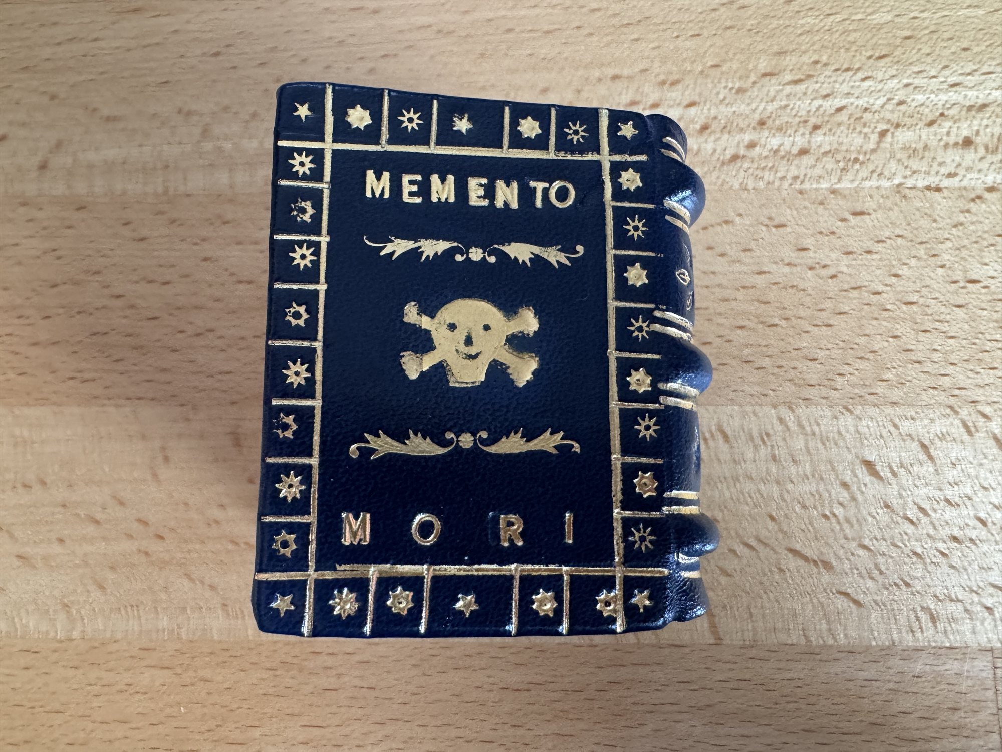 A dark green leather book cover gold-tooled with MEMENTO above a skull and crossbones and MORI below, bordered in stars