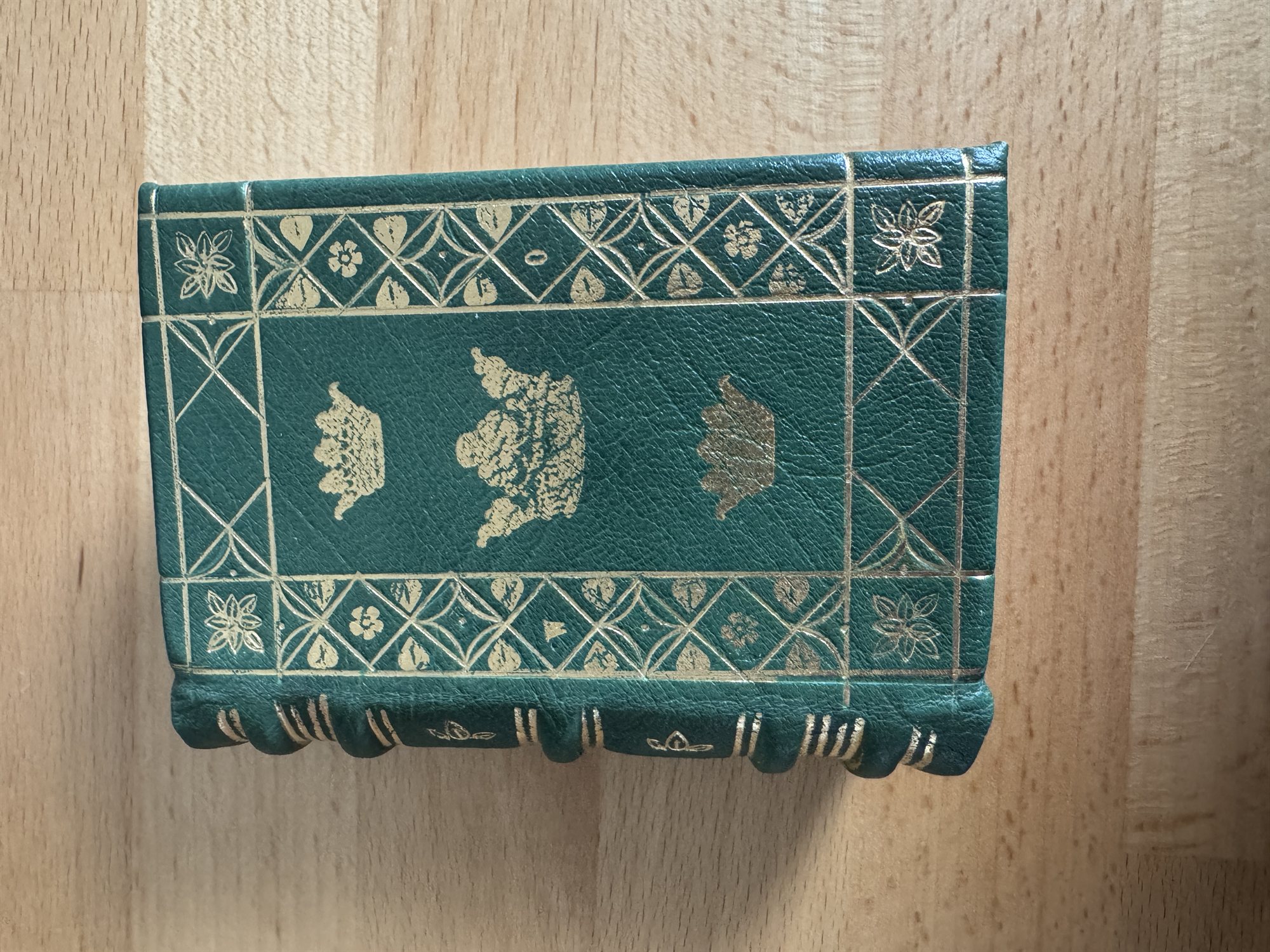 A green leather book cover tooled with a diamond lattice border framing three gold-stamped crowns of increasing size stacked down the center
