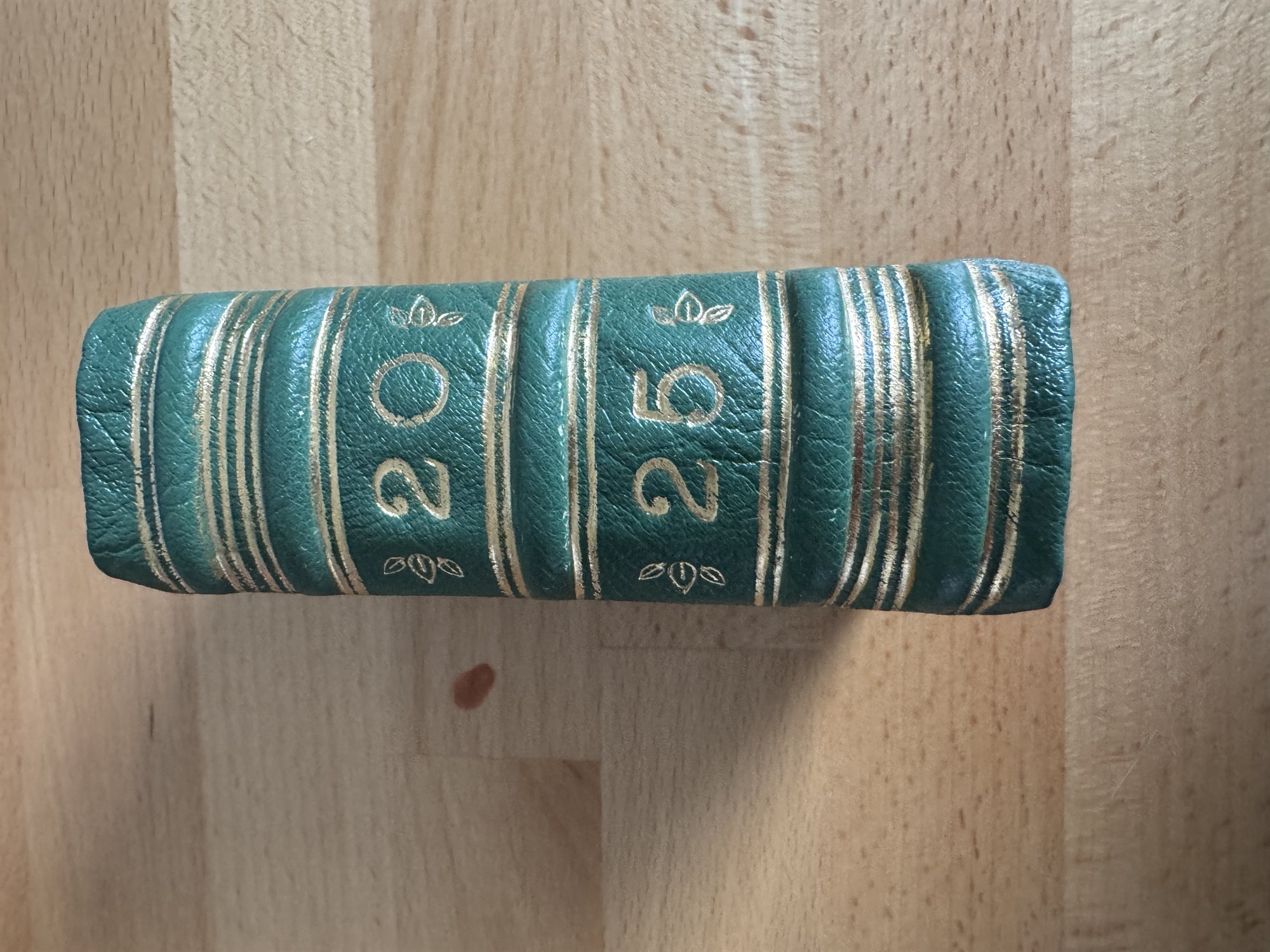 The spine of a green leather book gold-tooled with 20 and 25 separated by floral devices between raised bands