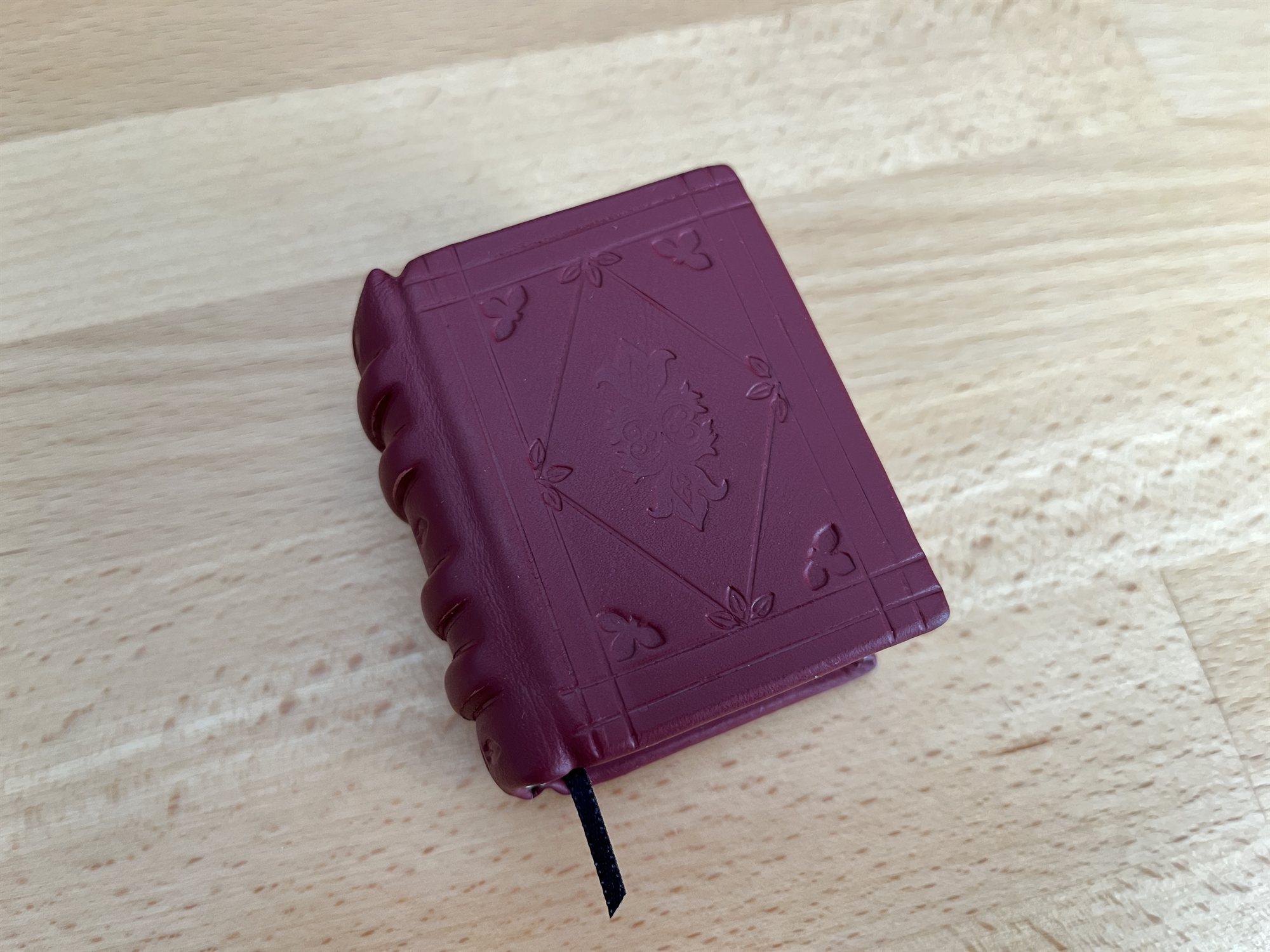 A burgundy leather book standing upright with its blind-tooled diamond cover and a black ribbon marker trailing from the pages