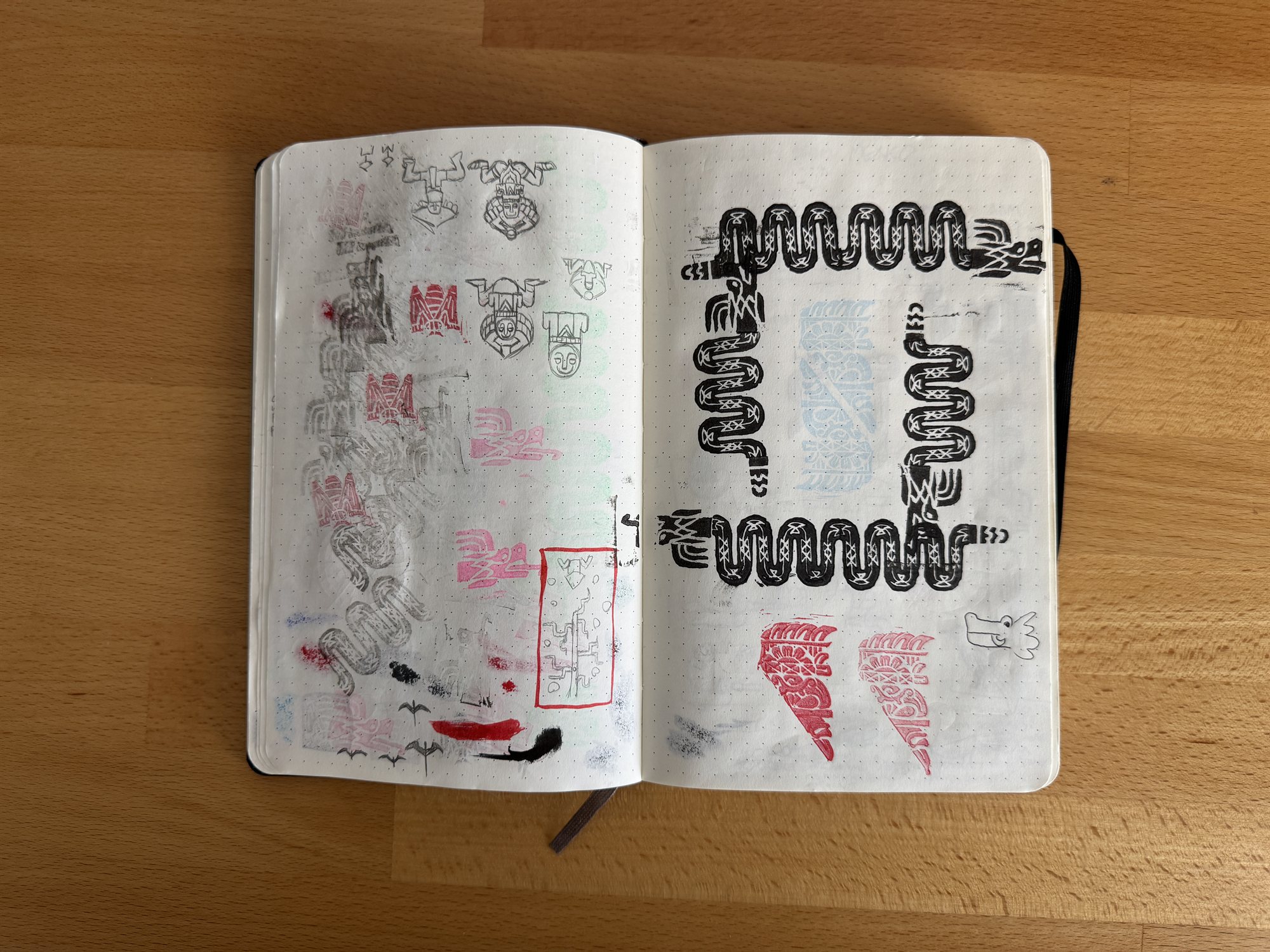 A sketchbook spread of pencil studies for deity head glyphs beside inked test prints of the woven step-fret border pattern