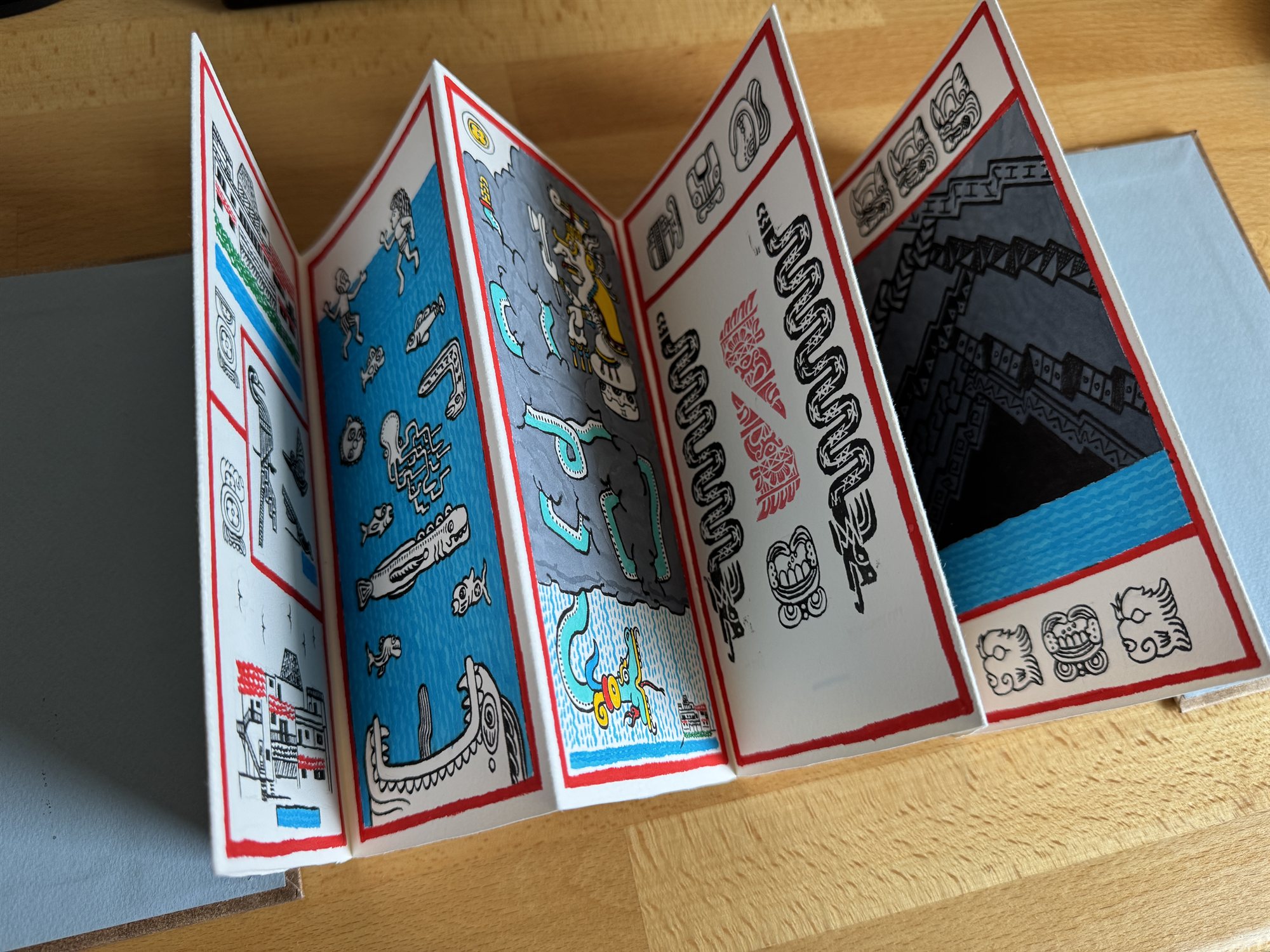 The accordion-fold codex fully unfolded and standing upright in a zigzag, six painted panels visible in sequence from a building and shoreline scene through an underwater dive, a storming rain god, a glyph key, and a woven step-fret pattern