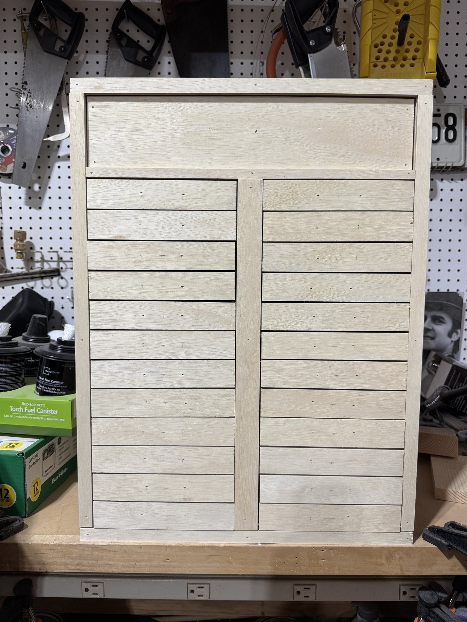 The cabinet's front panel with case openings framed out in pale wood strips, ahead of the pulls and trays being installed