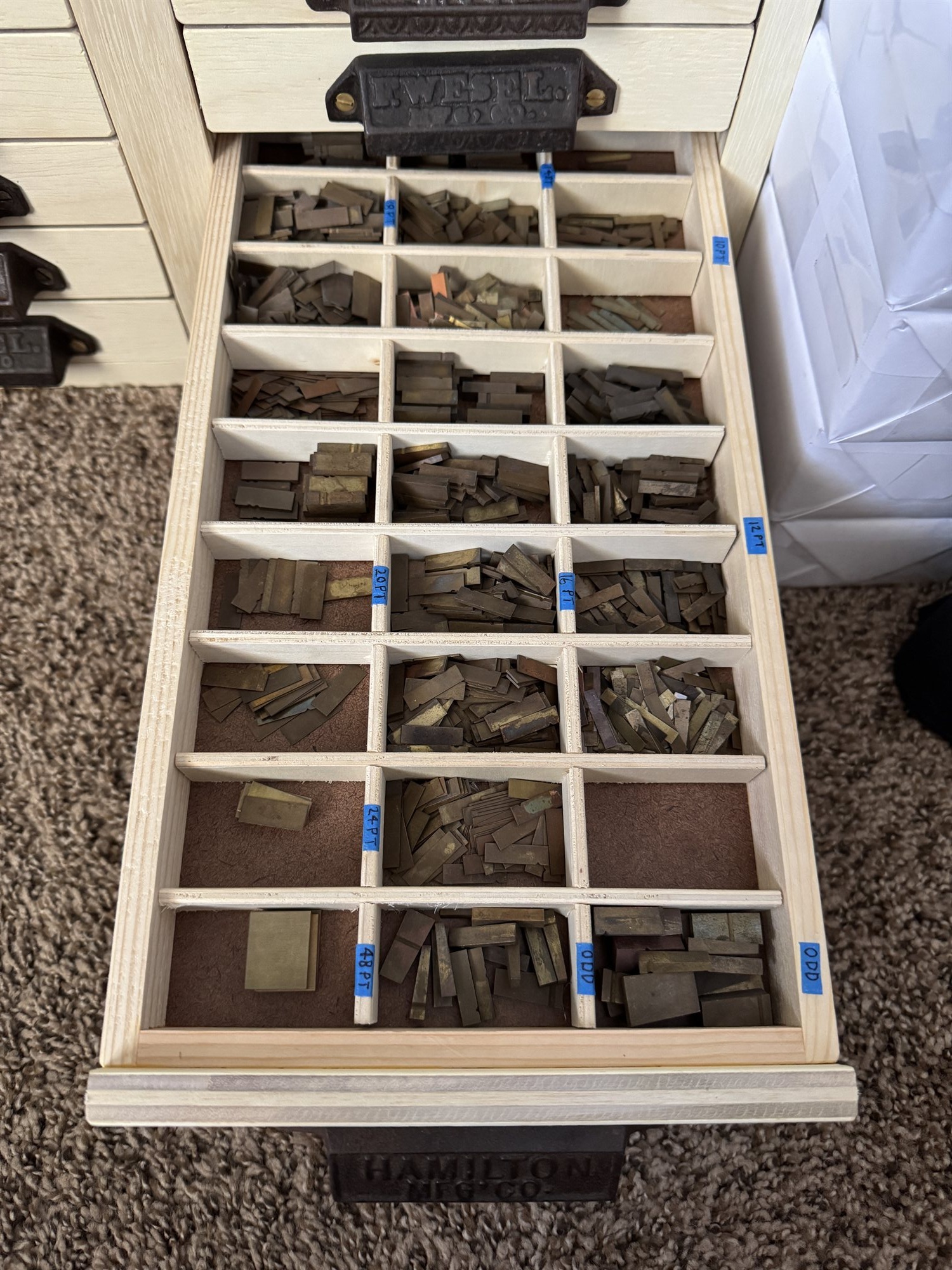 Overhead view of a case tray's compartments, each hand-labeled by point size — 10PT, 12PT, 16PT, 20PT, 24PT, 48PT, ODD — and filled with loose brass type sorts