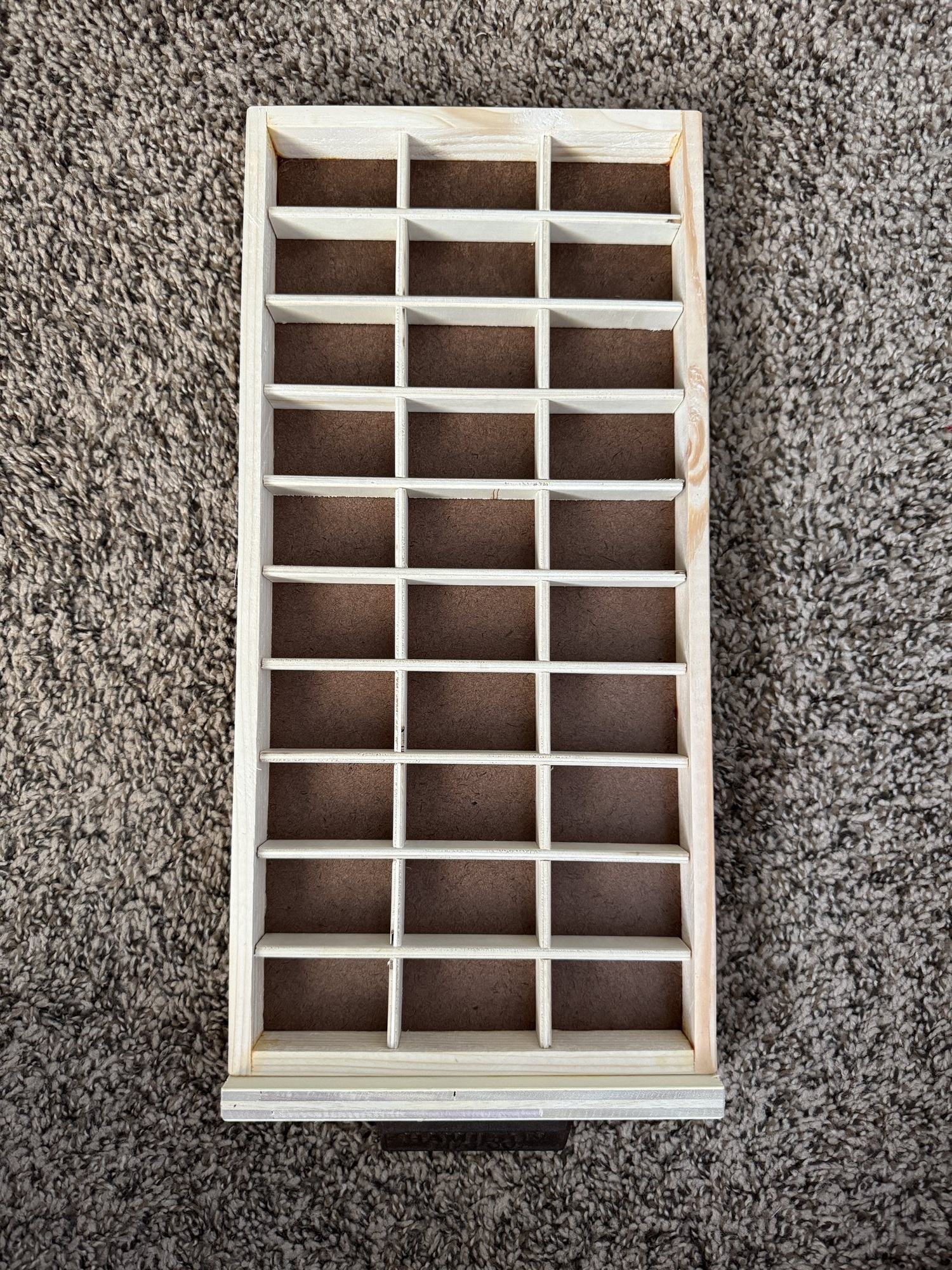 Close overhead view of an empty case tray's grid, thirty small compartments divided by thin plywood strips