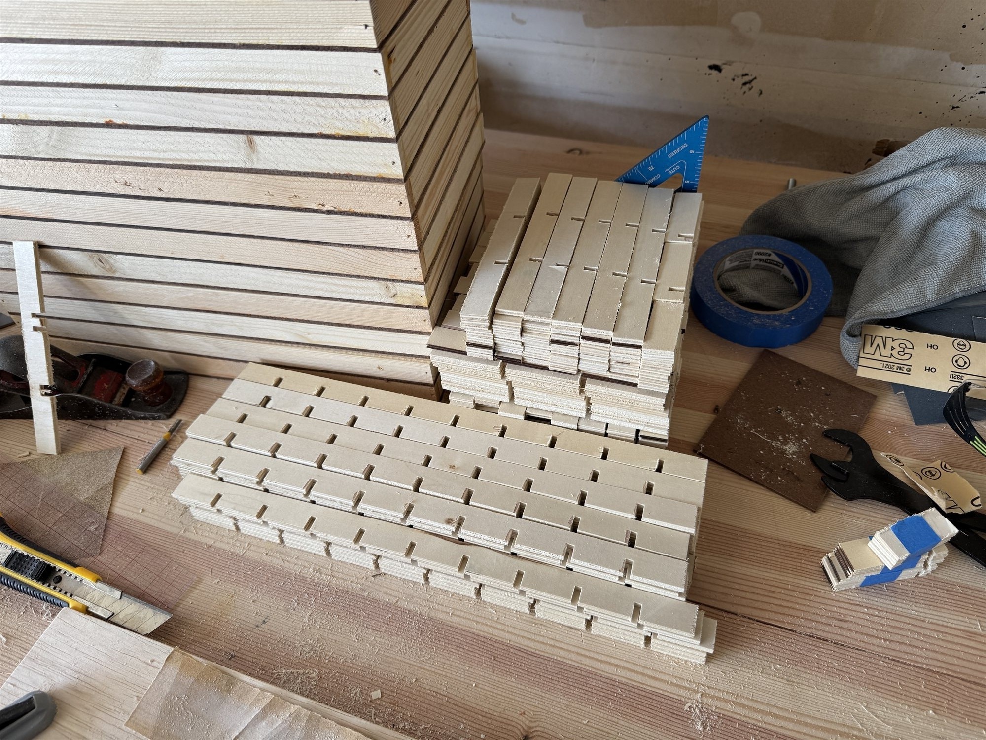 Rows of divider strips with evenly spaced notches cut for interlocking assembly, laid out on the workbench next to a speed square and utility knife